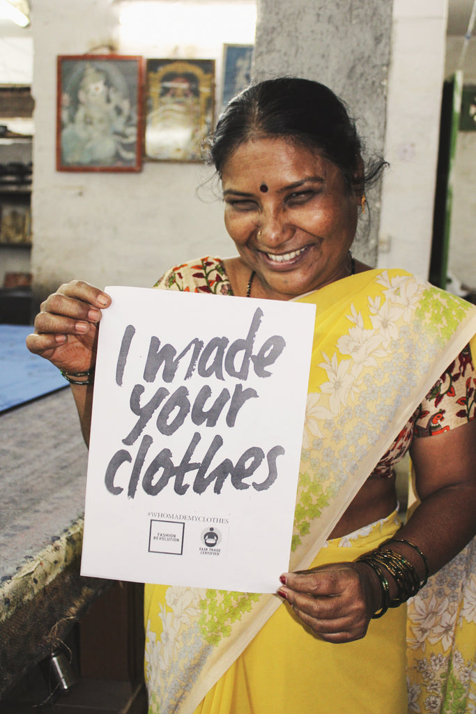 An Indian garment worker holds a sign that says "I made your clothes"