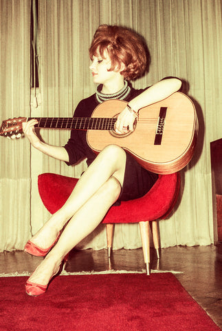 A woman from the 1960s strumming an acoustic guitar and wearing a minidress, whose hemline is above the knee and reflects the feminist political fashion trends of the time.