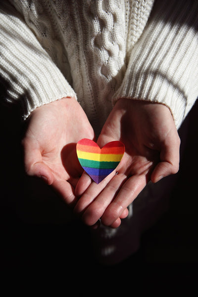 Two hands holding rainbow colored paper heart