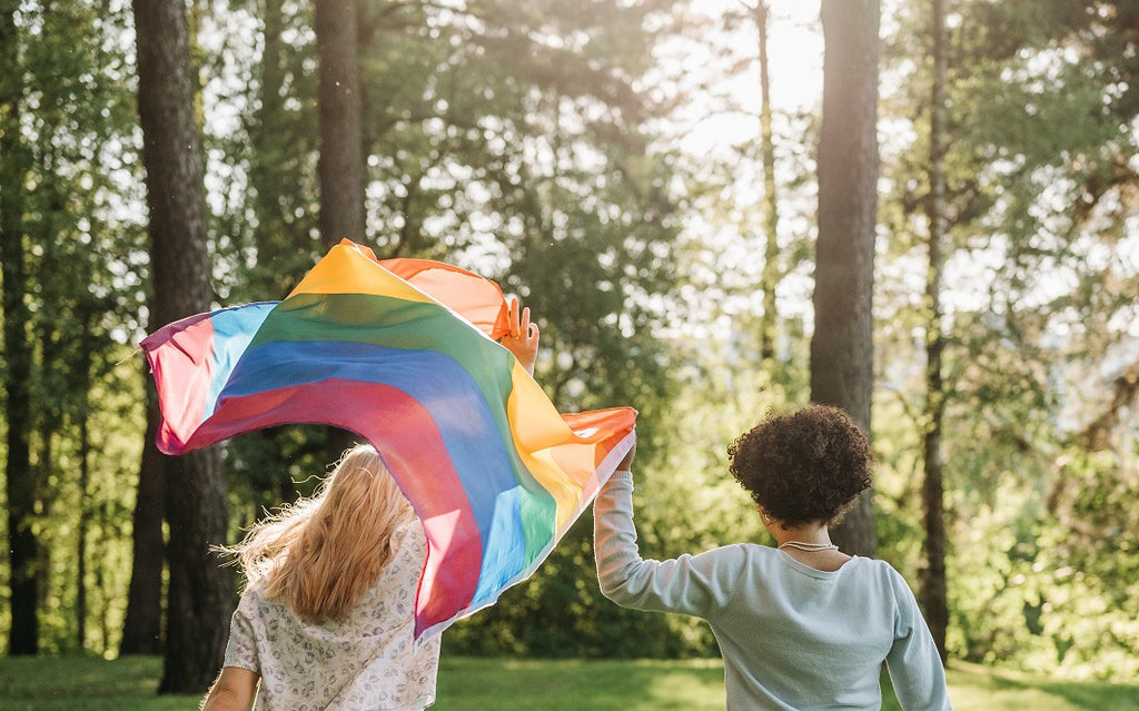 Two women hold rainbow flag in front of greenery