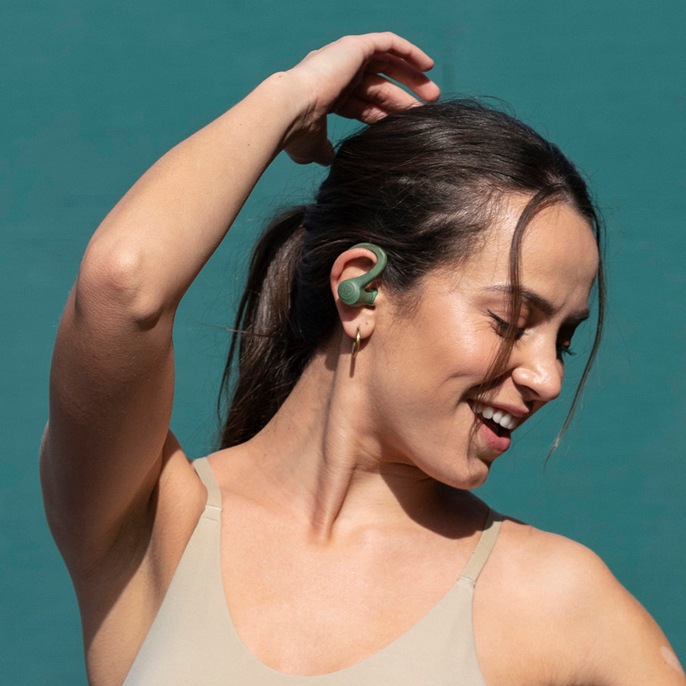 Frau mit GO Air Sport True Wireless Earbuds in Grün mit erhobenem Arm, als würde sie tanzen