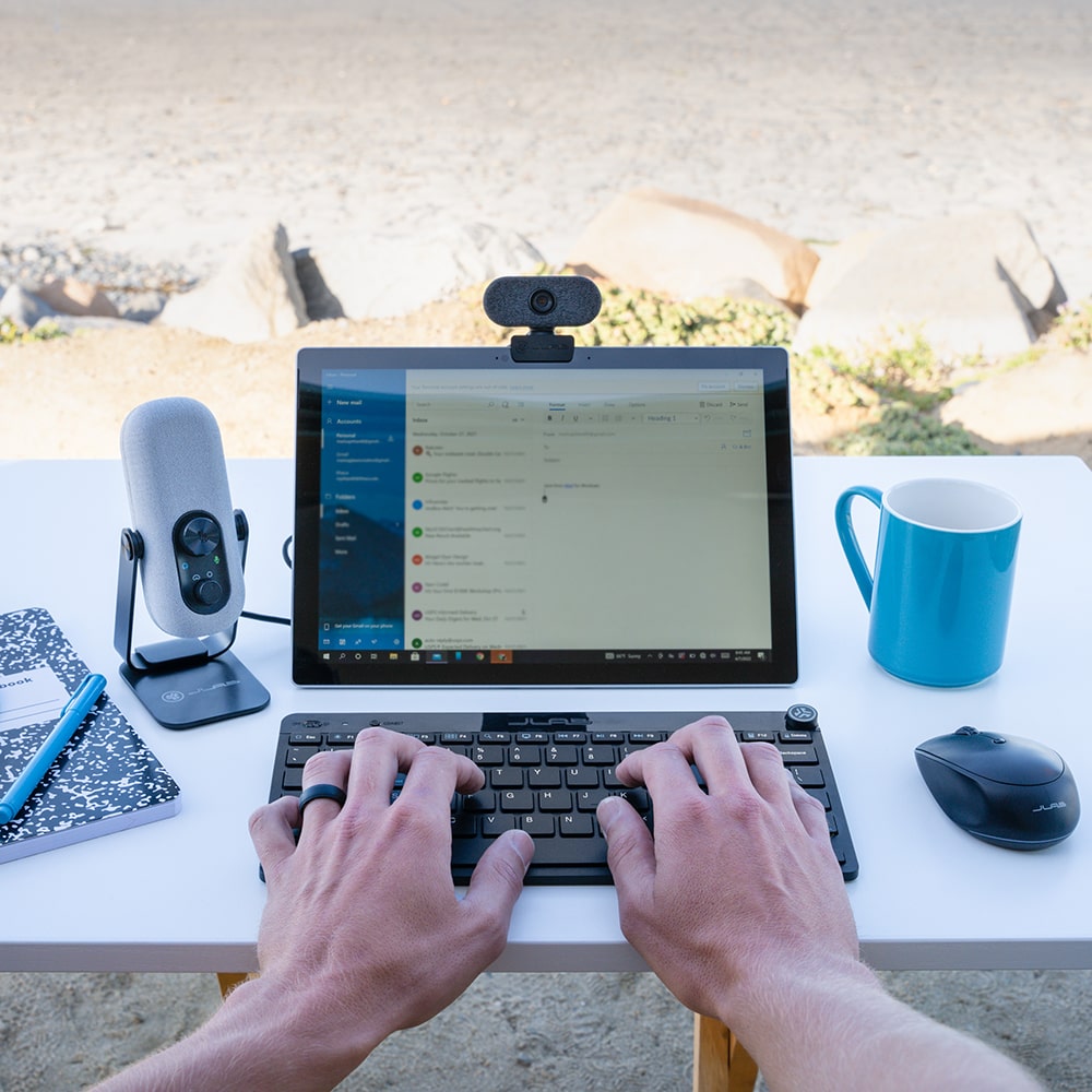 Hands typing on a keyboard on a table with Go CAm and JLab microphone