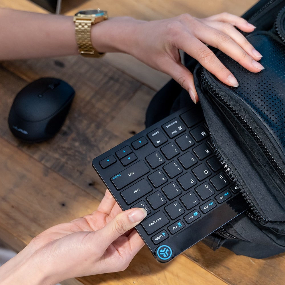 Hand putting GO Keyboard into a black backpack on a table