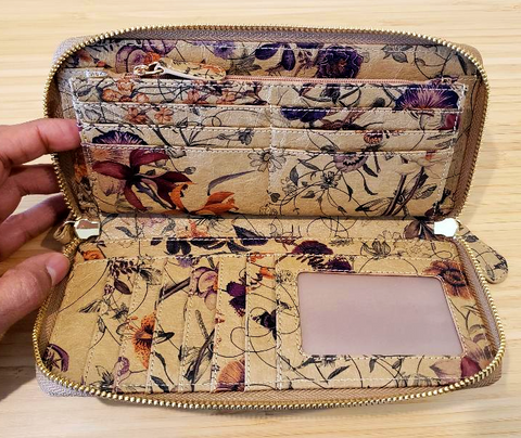 The interior of a zippered wallet made from a tan paper with a floral pattern. The interior includes serveral card slots, an ID card slot, and a zippered pouch.
