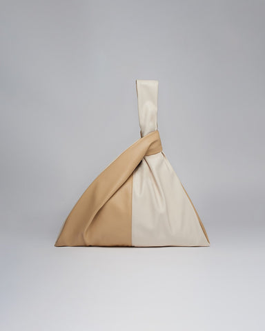A bag with tan and beige panels whose handles knot through each other as a closure.