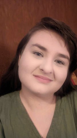 A selfie of a white woman with long brown hair, wearing a green v-neck blouse. She is wearing simple, natural makeup, and smiling at the camera.