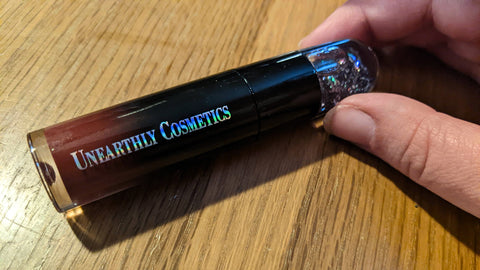 A tube of liquid lipstick. It is a gradient of mauve to black that finishes in a glittery cap.