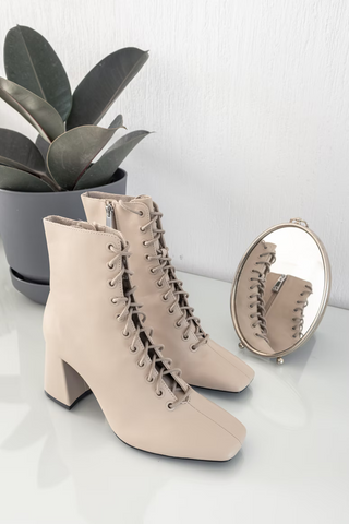 A pair of lace-up light beige boots with thick, short heels.