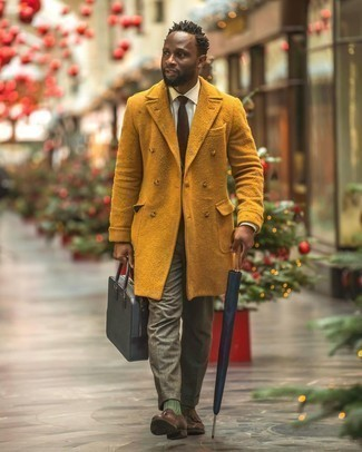 A man in business attire with a mustard yellow overcoat carries a charcoal gray briefcase by its top handles.
