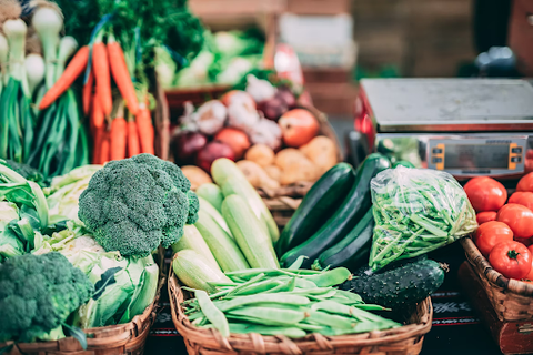 A variety of vegetables on a market stall, such as broccoli, carrots, tomatoes, cucumber, and peas.