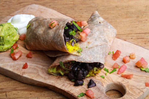 A breakfast burrito with eggs, black beans, and tomatoes, split in half.