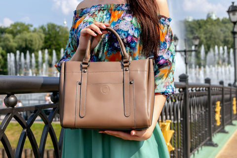 A woman in a bright floral top holds a small brown tote up to the camera.