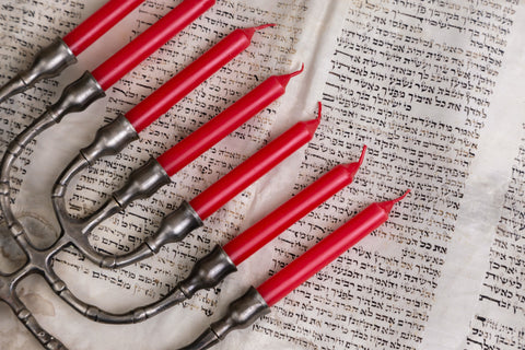 A menorah with red candles lays on an open Torah.