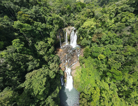 An overhead shot of a waterfall surrounded by green trees.