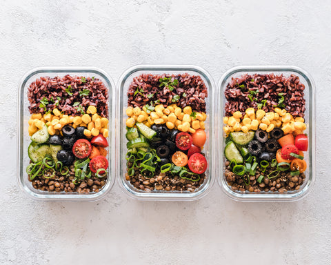 A set of three glass containers with a varity of vegetables packed in them.