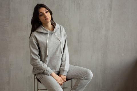 A woman in a grey sweatsuit sits in front of a grey background.