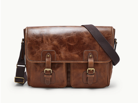 A brown messenger bag with brass hardware, a black fabric strap, and two front pockets.