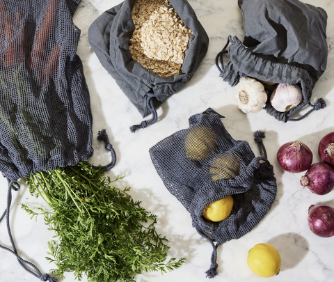 A set of black mesh produce bags containing oats, garlic, lemons, and herbs.