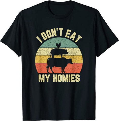 A black t-shirt with a block color illustration showing the silhouettes of a chicken standing on a pig standing on a cow. Text in an off-white block text reads "I don't eat" above and "my homies" below.