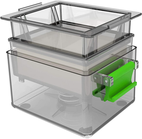 A tofu press; a rectangular, clear, plastic device with several pieces that fit together. It has green handles.