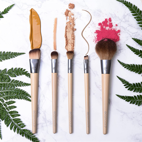 A set of five makeup brushes (from left to right, a concealer or foundation brush, a rounded fluffy brush, a flat blending brush, a small angled brush, and a blush brush) made of bamboo, metal, and tan and brown bristles.