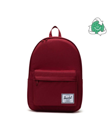 A red two-pocket backpack with a small white logo stamp on the bottom right corner of the front pocket.