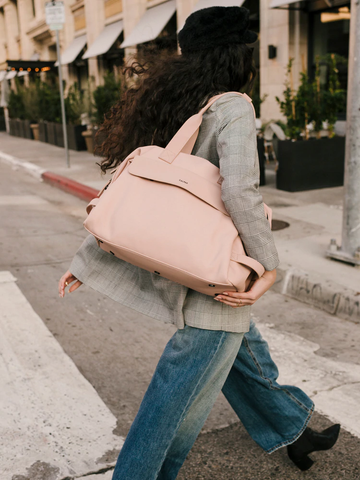 A woman in jeans and a blazer carrying a light pink weekender tote.