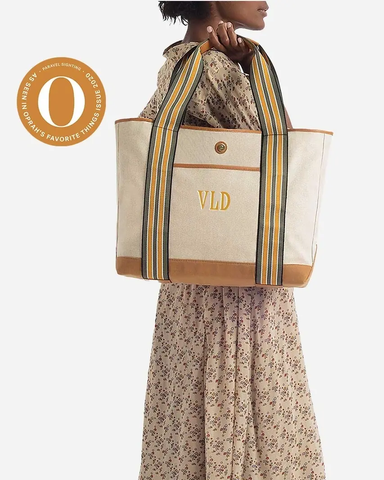 A woman in a boldly-patterned yellow dress carries a white canvas weekender tote.