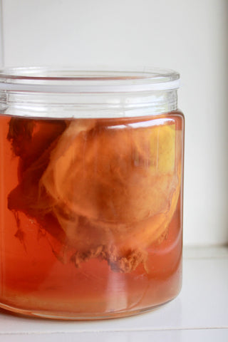 A glass jar containing an orange liquid with a whitish, stringy solid floating in it.