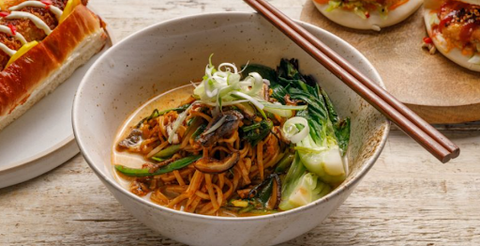 A bowl of noodles with vegetables and chop sticks.