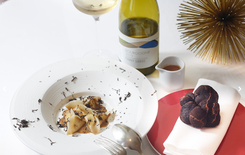 An upscale restaurant meal sprinkled with grated truffle and paired with a white wine.