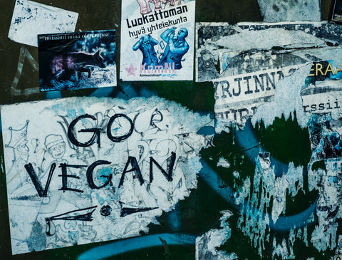 A bluescale image with graffiti that reads "Go Vegan" on a concrete wall plastered in posters.