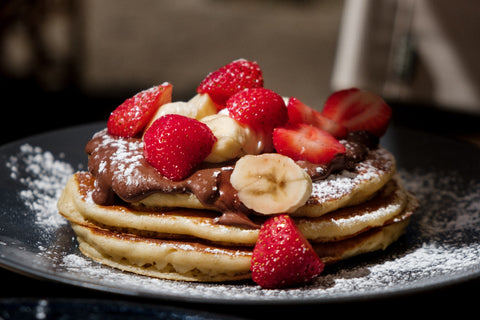 A stack of pancakes topped with Nutella, strawberries, and bananas.