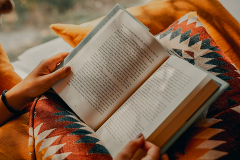 An open hardback book being held on a patterned pillow in someone's lap.
