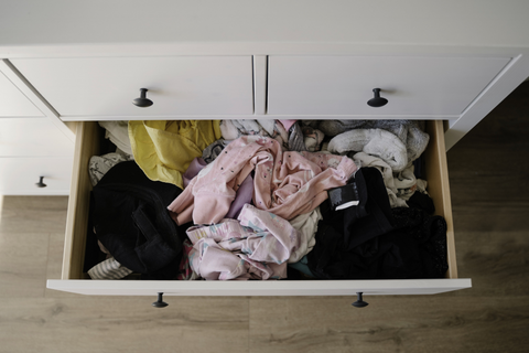 A set of white dresser drawers, one of which is pulled open to reveal unfolded clothes.