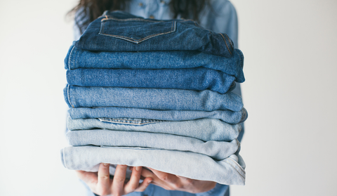 A woman holds a stack of blue jeans in various fades.