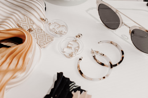 A flatlay of several tan and brown accessories inlcuding earrings and sunglasses.