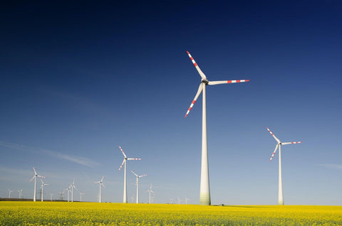 Energy windmills on a green field against a blue sky.