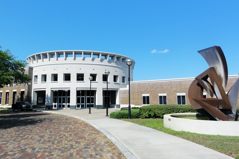 The front of the Orlando Museum of Art; a large, white, round structure with many windows and double door entrances. A modern art sculpture is on the right hand side.