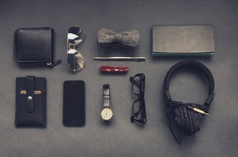 A flatlay of various accessories including a wallet, sunglasses, cardholder, watch, and headphones.