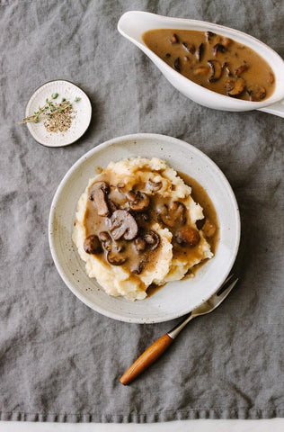 A bowl of mashed potatoes topped with mushrooms and thick brown gravy.
