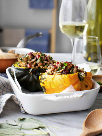 A white casserole dish containing stuffed green and yellow acorn squash.