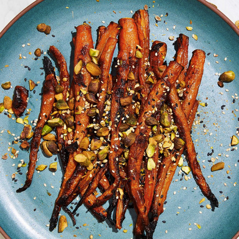 A blue ceramic plate holds orange roasted carrots covered in various nuts and spices.