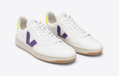 White casual sneakers with a violet "V" shaped accent mark on the arch and outer side.