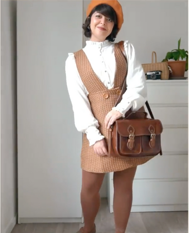 A woman in a brown dress and white sweater, holding a brown satchel bag.