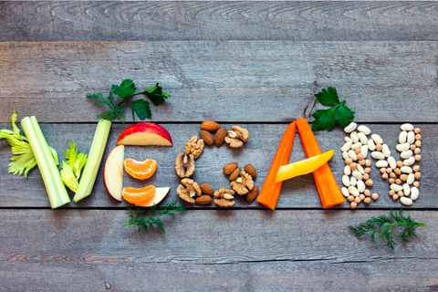 The word "Vegan" spelled out in various fruits, nuts, and vegetables.
