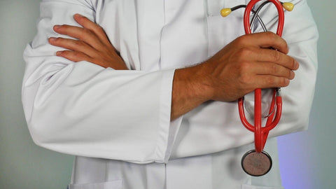 A close-up of a person dressed in a doctor's coat with folded arms. Their left hand holds a stethoscope.