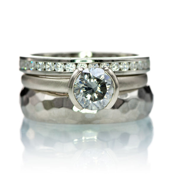 Ring stack with gray moissanite center, a wide hammered band and channel set moissanite eternity ring