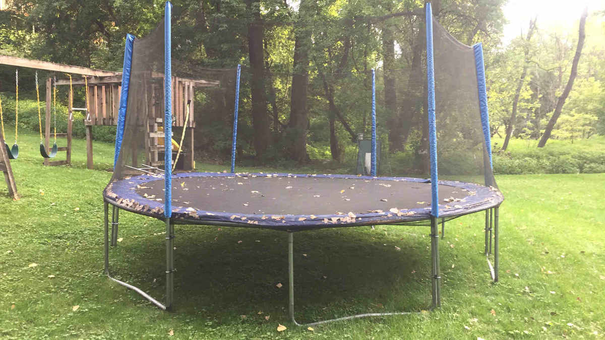A cheap trampoline with leaves on the mat in a backyard.