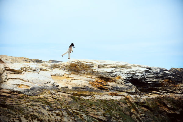 Terumi walking along the rocky shore getting fresh air, exercise and quiet which calms her stress benefiting gut to skin health.